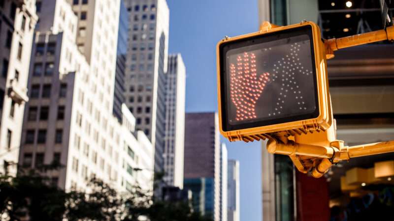 A halt sign on a city crosswalk light with skyscrapers in the background |  Andrey Bayda/Dreamstime.com