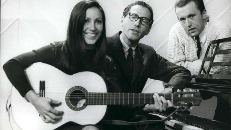 Tom Lehrer on the piano alongside guitarist Julie Fox and host David Frost on the set of the Frost Report on March 3, 1966. | Keystone Pictures USA/ZUMAPRESS/Newscom
