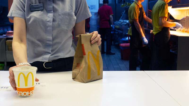 An employee serves a drink and a paper bag on a McDonald's counter | Photo: Vladimir Zuev/Alamy