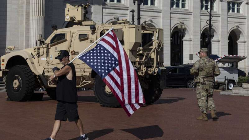 Members of the National Guard carrying sidearms and a man carrying an upside-down American flag stand outside Union Station in Washington, D.C., in September 2025. | Mehmet Eser/ZUMAPRESS/Newscom