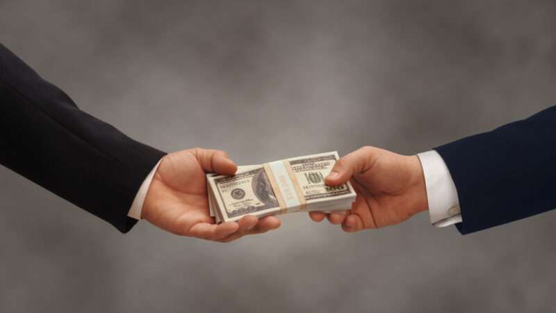 Two businessmen pass a stack of $100 bills. | James Group Studios, Inc. | Dreamstime.com