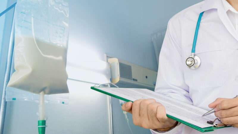 A doctor holds a clipboard by an I.V. pole. | Kanokwan Sangmontian | Dreamstime.com