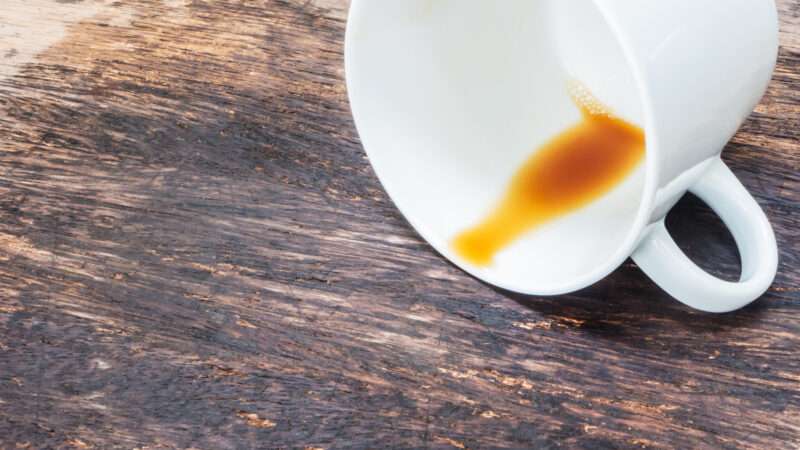 Coffee cup tipped over with coffee spilled out on a wood surface. | Pkanchana | Dreamstime.com