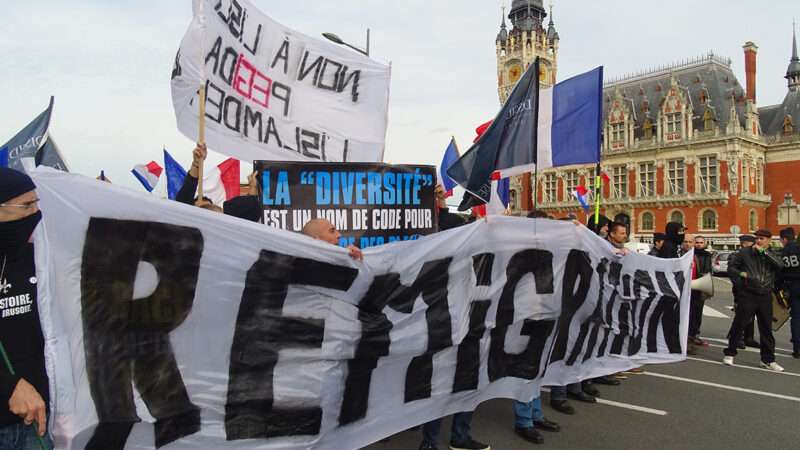 Protesters carrying a larger banner that says 'remigration' | Photo: An anti-immigration protest in Calais, France, in 2015; Jérémy-Günther-Heinz Jähnick/Wikimedia