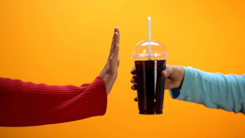 A woman holds up her hand to decline a sugary beverage from a friend. | motortion | Dreamstime.com