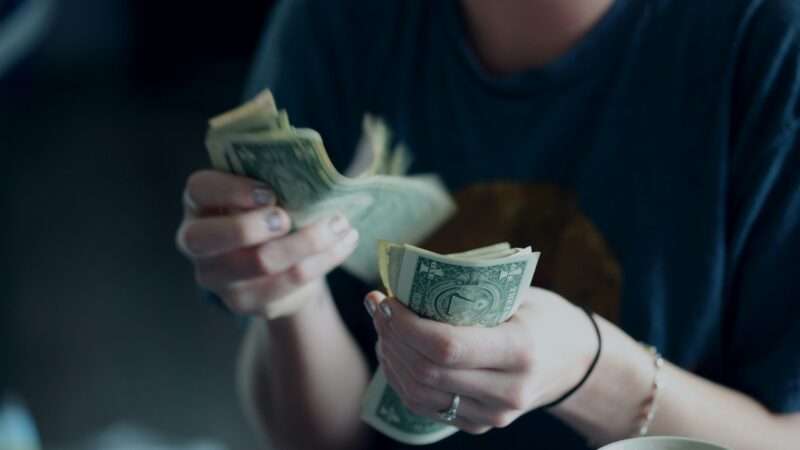 Someone counting a stack of dollar bills | Photo by <a rel=