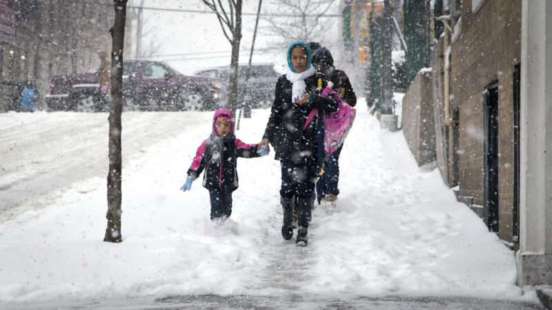 A family wearing winter clothing walks down a sidewalk in heavy snow. | Eddie Toro/Dreamstime