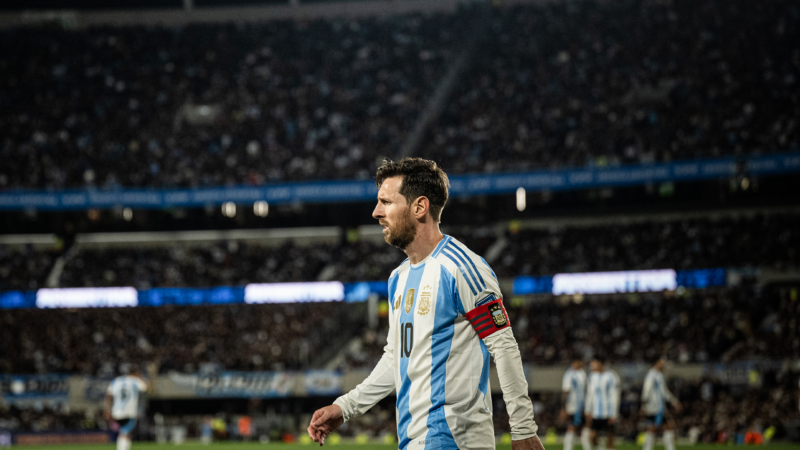 Lionel Messi walking on a soccer field, with several other Argentina players in the background, and three full tiers of stadium seating behind them. | Manuel Cortina / SOPA Images/Sipa USA/Newscom