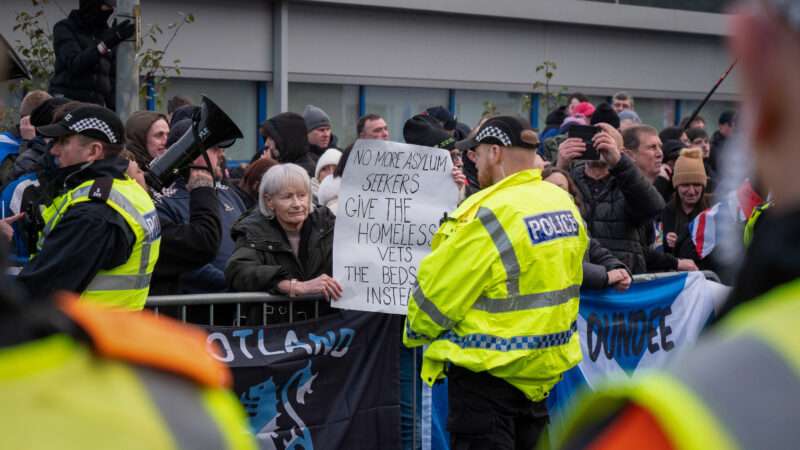 Police in Scotland at a protest outside the Cladhan Hotel. A demonstrator holds a sign that reads, "No more asylum seekers, give the homeless vets the beds instead." | Cameron Scott/ZUMAPRESS/Newscom