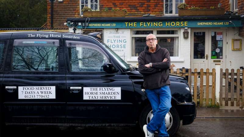 A man leans against a black cab with signs on the side that read, 