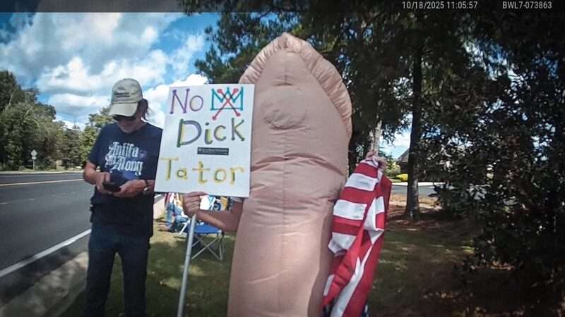 Bodycam footage of Renea Gamble at an October 2025 No Kings protest, wearing an inflatable penis costume and holding a sign that says "No Dick-Tator." | Fairhope Police Department