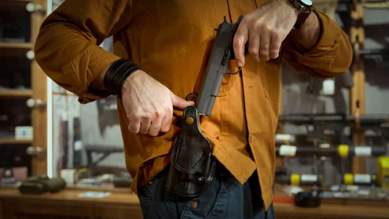 A man in a gun store pulls a semiautomatic handgun from a holster. | Ingram Publishing/Newscom