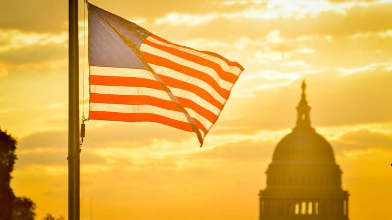 The American flag flaps in the breeze at dusk. The dome of the U.S. Capitol is visible in the distance. | Orhan Çam/Dreamstime