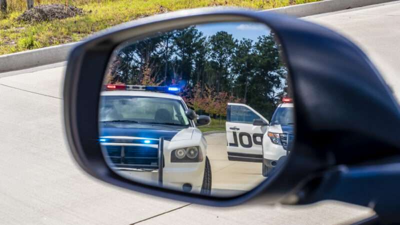 Police cars with lights on are seen in a rearview mirror. | Photo:Walter Arce/Dreamstime