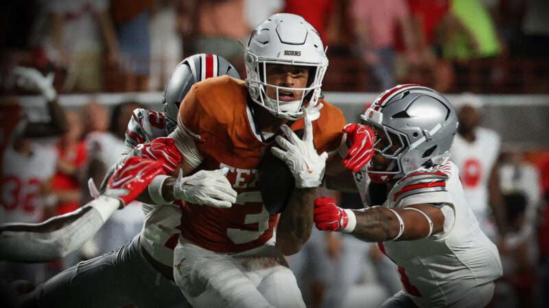 A football player in an orange Texas jersey holds the ball and tries to escape a few players in white Ohio State football jerseys that are trying to tackle him. | David Buono/Icon Sportswire DCV/David Buono/Icon Sportswire/Newscom