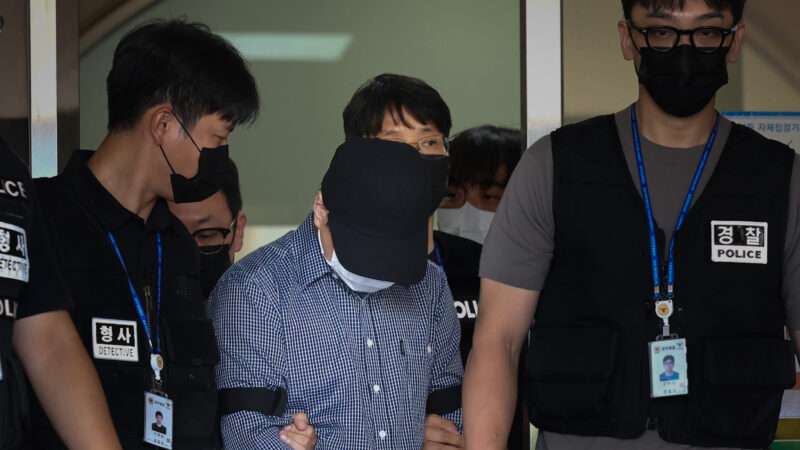 South Korean police officer only identified by the surname Bu. His head is down and he wears a dark blue baseball cap as officers lead him away in handcuffs. | Yonhap News/YNA/Newscom