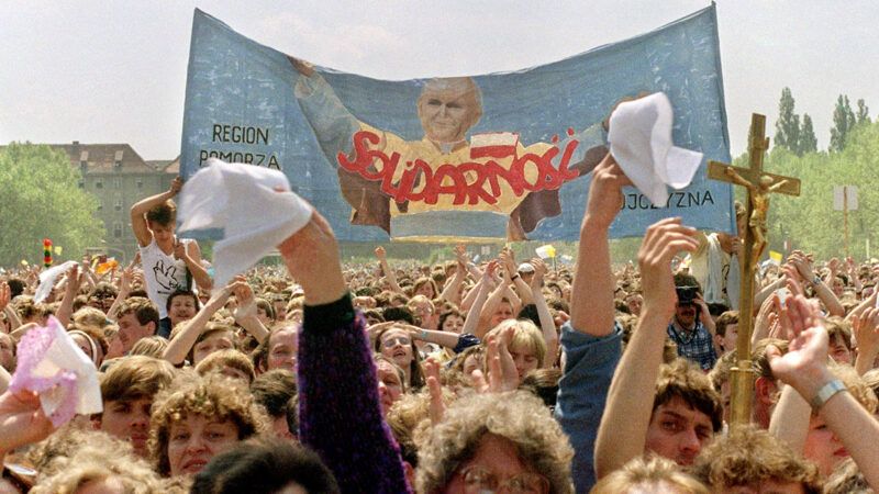 slade | Photo: Supporters of the outlawed Solidarity trade union wave a banner during the pope’s 1987 trip to Poland. Marcel Mochet/AFP/Getty