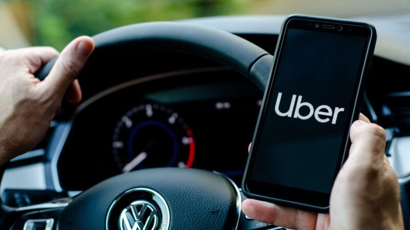 Hands holding the steering wheel and a smartphone with the Uber screen on it | Oleksandr Lutsenko/Dreamstime.com