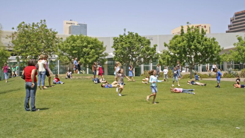 Elementary school students running around a park under a blue sky.