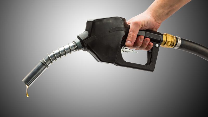 Hand holding a dripping fuel pump in front of a spotlit gray background