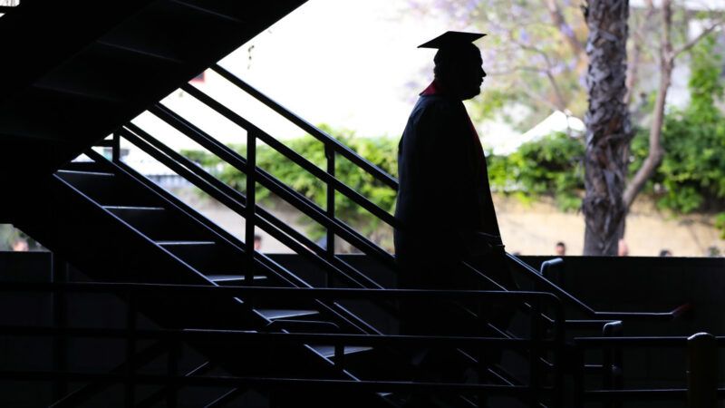 College student in cap and gown stands in the shadow