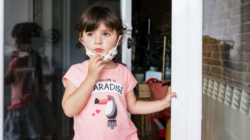 A toddler takes off her face mask.