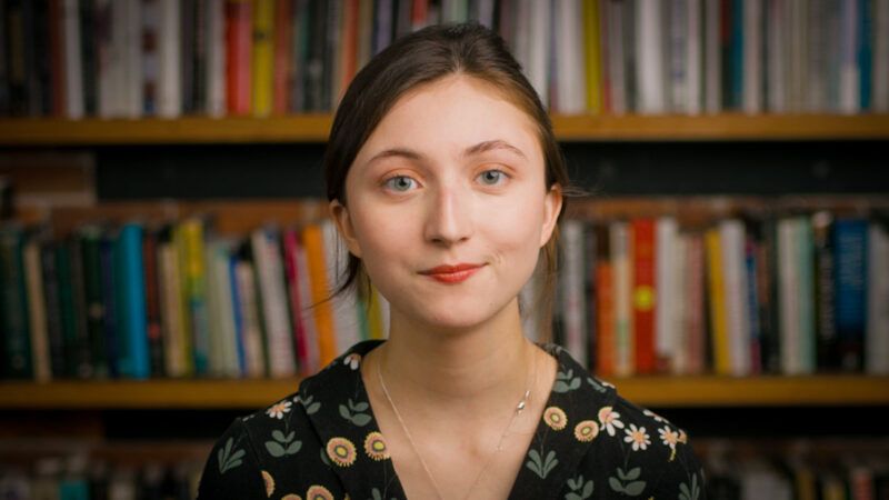 Image of Reason's Emma Camp in front of bookshelves