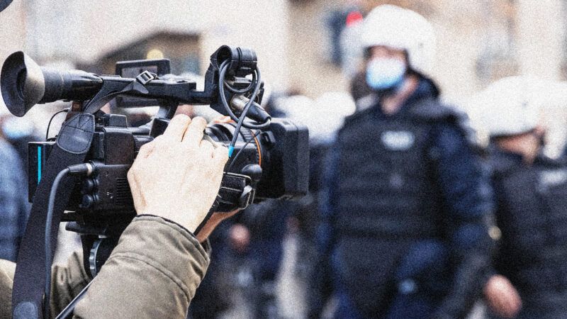 An image of a TV camera filming police in riot gear