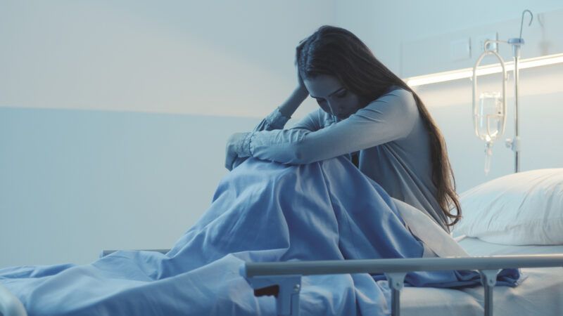 Stock photo of a woman with long hair, sitting in a hospital bed and looking upset. Stock photo of a woman with long hair, sitting in a hospital bed and looking upset.