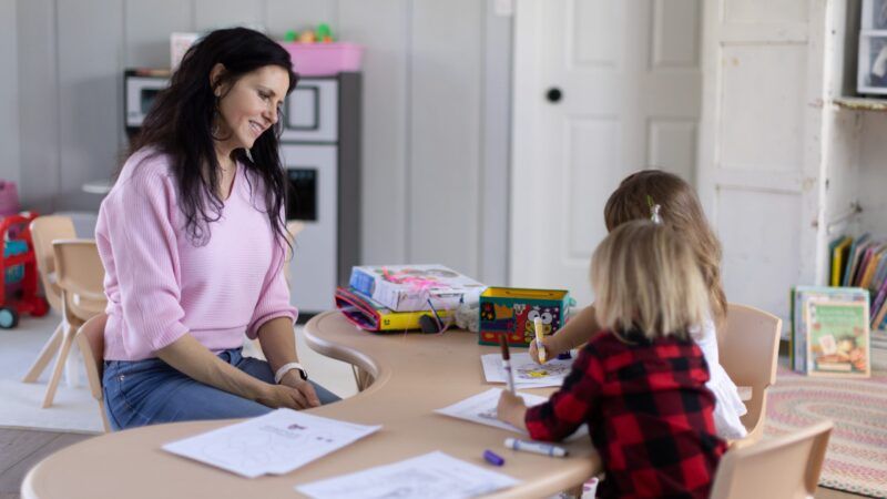 Woman sitting at a table with two small children who are coloring. | Institute for Justice