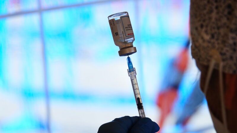 a health worker holds a needle into a bottle with a vaccine dose