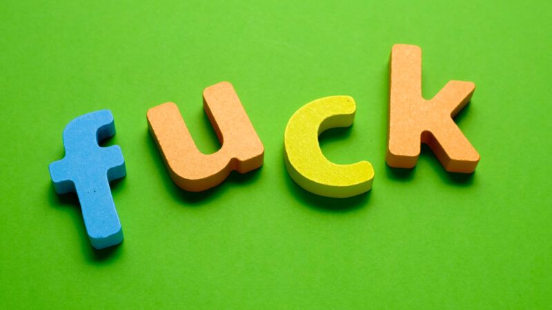 Multicolored wood letters spelling "fuck" on green background.