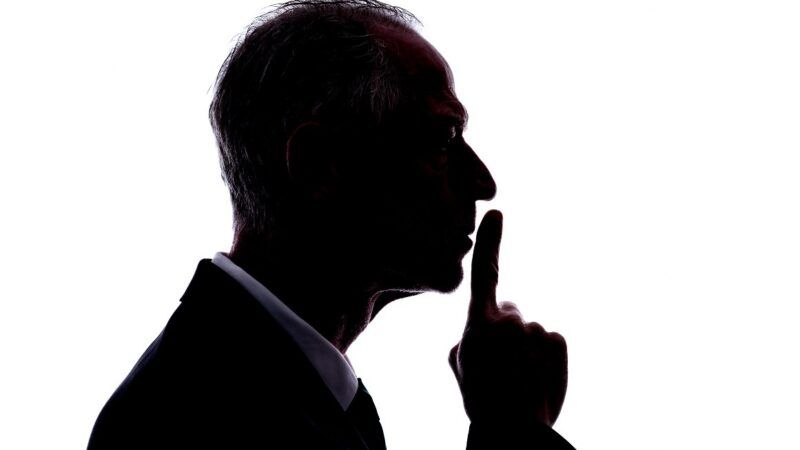 Profile of a man holding a finger up to his mouth in a gesture for silence against a white background
