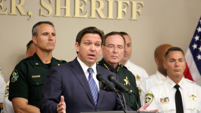 Florida Governor Ron DeSantis speaks at a podium as law enforcement officials stand behind him at a press conference