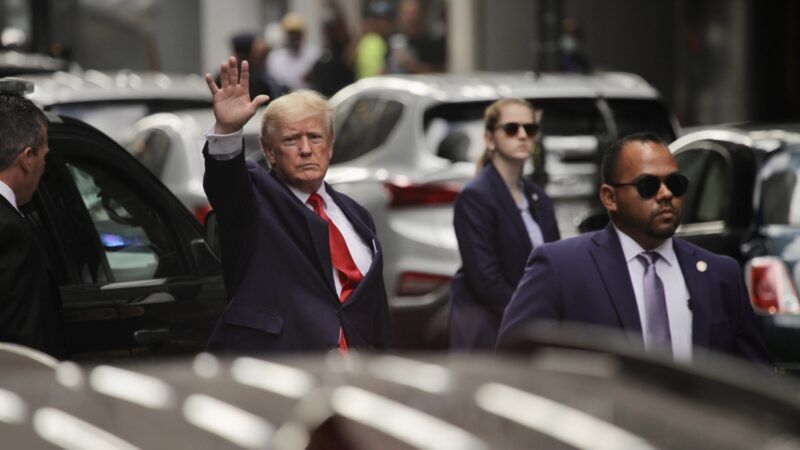 Trump waves at camera from the street while leaving an office