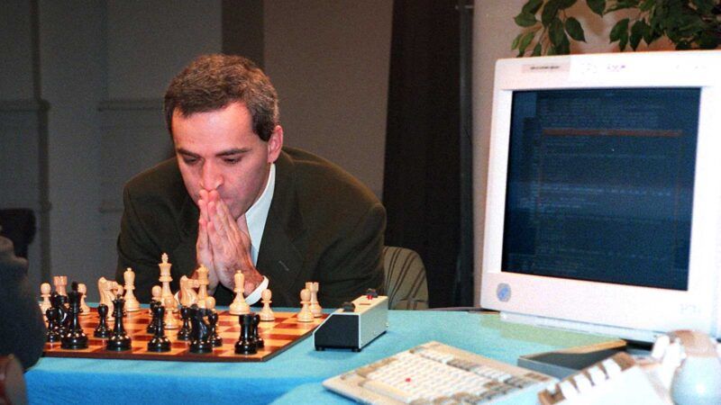Garry Kasparov with chess board on left side of the image, while an old computer is on the right.