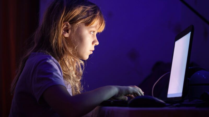 a young girl uses a laptop alone in a dark room
