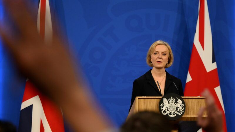 Prime Minister Liz Truss stands at a podium in front of two British flags.