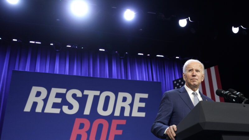 Joe Biden in front of a sign that says "Restore Roe"
