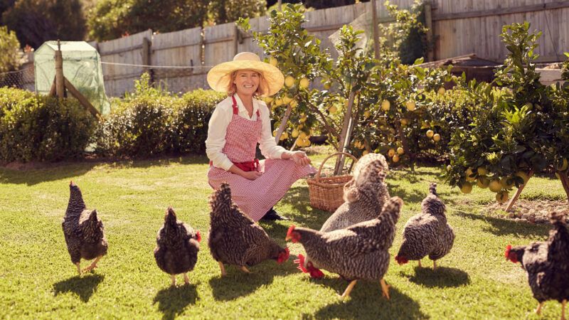 A woman in a sunhat poses with her backyard chickens.