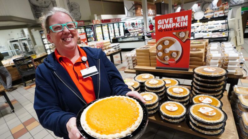 A grocery store worker is seen holding a pumpkin pie
