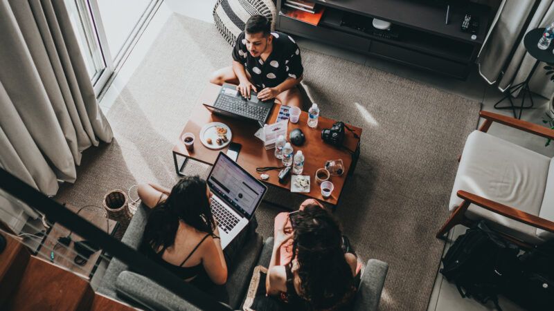 Three people on laptops working around a coffee table in a living room. | Matheus Bertelli