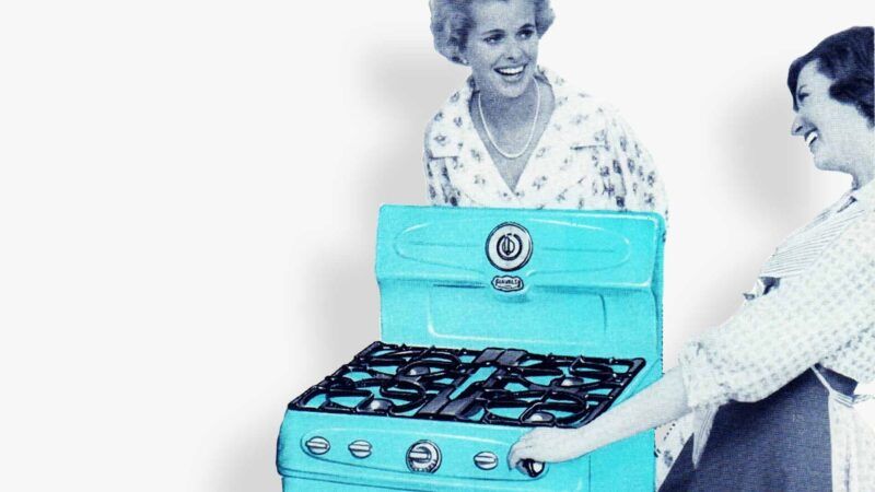 two woman standing around a gas stove