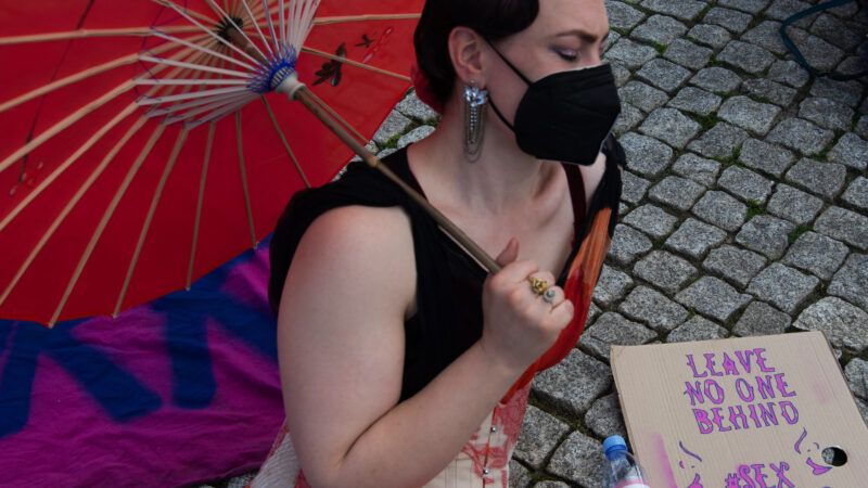 protester with red umbrella and a sign saying "leave no one behind | sex work is work" | Paul Zinken/dpa/picture-alliance/Newscom