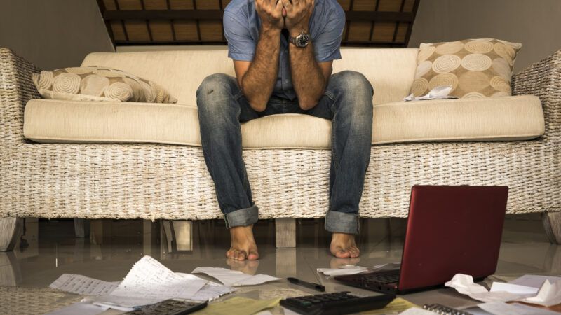 An exasperated young man covers his face in his hands as numerous financial documents litter the floor in front of him. | Marcos Calvo Mesa | Dreamstime.com