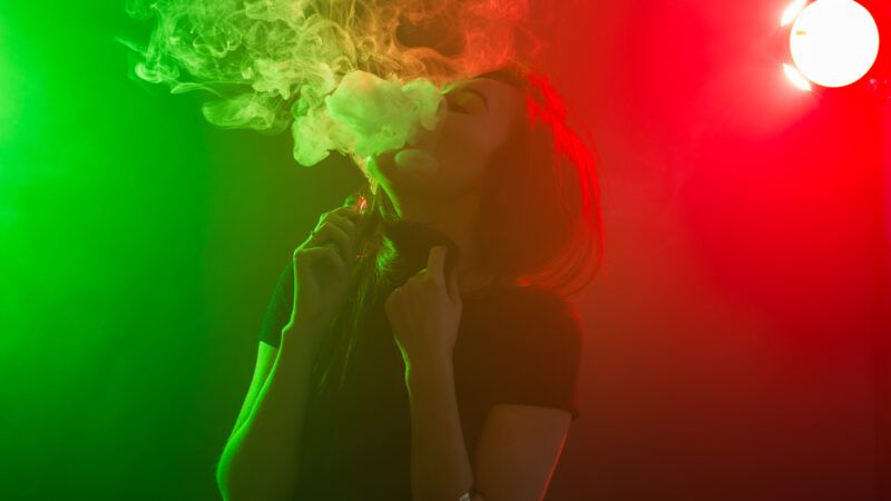 Woman smoking an e-cigarette in front of neon lights