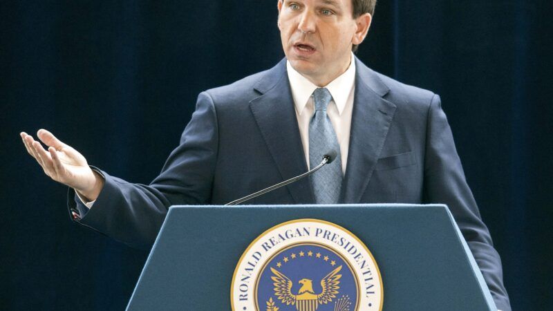 Ron DeSantis speaks behind a podium against a dark background