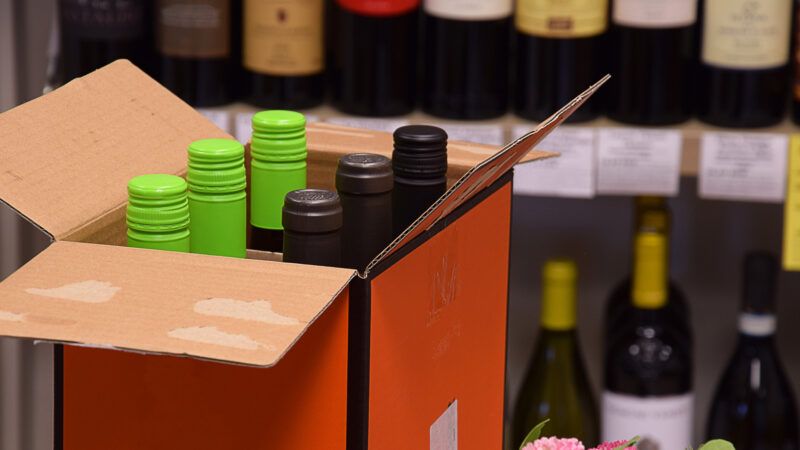 Box of wine bottles in front of a shelf with wine