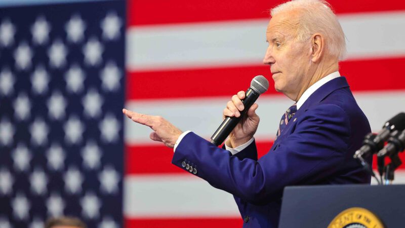 President Joe Biden addresses a crowd, in front of an American flag and next to a lectern bearing the presidential seal.