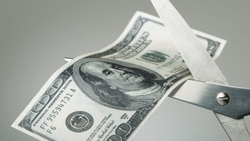 A pair of scissors cuts through a $100 bill. | Pogonici | Dreamstime.com